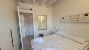 Une chambre à coucher avec un lit double, une table de chevet avec une lampe, un miroir et un mur orné d’une œuvre d’art florale.