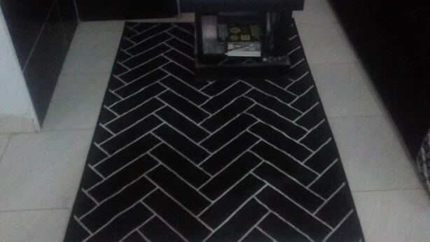 Cozinha pequena e moderna, com azulejos pretos e um tapete com padrão herringbone.