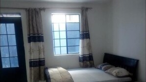 Une chambre à coucher avec un lit, une fenêtre avec des rideaux, une table de chevet et une porte.