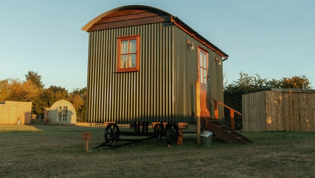 A small, single-story wooden structure with a sloped roof, a front porch, and a small porch area. - Glamping in Wiltshire in our Luxury Shepherds Hut (Chippenham)