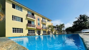 Un hotel con piscina, varios balcones y un cielo azul despejado.