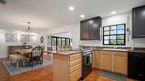 A modern kitchen with a central island, wooden cabinets, and a black dishwasher. - ‘Our Encanto’ -quiet golf course view-Tampa suburb (Valrico)