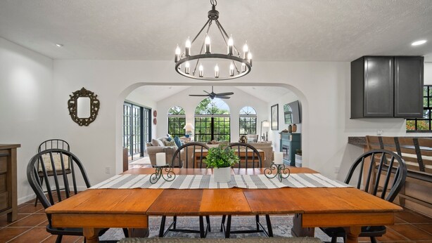 A spacious dining area with a wooden table, black chairs, and a chandelier. There is a view of a kitchen and a living area with a ceiling fan. - ‘Our Encanto’ -quiet golf course view-Tampa suburb (Valrico)