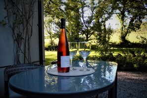 A table with a bottle and two glasses, set against a backdrop of trees and a grassy field. - Remarkable Apartment in Kenmare, Ireland (Sneem)
