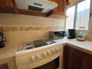 Una cocina con estufa a gas, microondas y licuadora sobre la encimera.