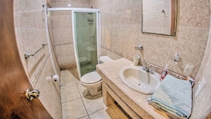 A bathroom with a glass shower enclosure, a toilet, a sink, and a mirror.