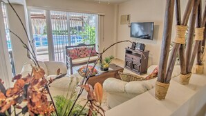 Una sala de estar con sofá, mesa de centro, televisión y un balcón con vistas a zonas verdes.