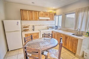 A compact kitchen with wooden cabinets, a white refrigerator, a stove, and a round glass table with chairs. - Perla 61: Groundfloor 2BR w Pool - 6 blocks to Beach (Bucerías)