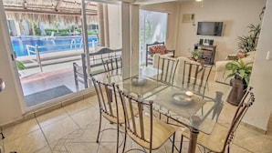 A dining area with a glass table and chairs, a TV, and a sofa with a plant.