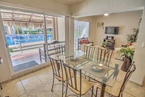 A dining area with a glass table and chairs, a TV, and a sofa with a plant.