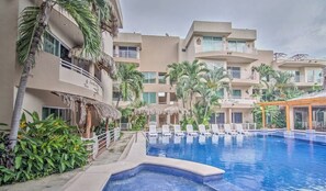 A hotel with a swimming pool, palm trees, and a thatched-roof structure. - Perla 61: Groundfloor 2BR w Pool - 6 blocks to Beach (Bucerías)