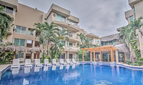 Un hotel con piscina rodeada de palmeras y sillas de descanso.