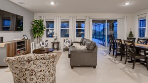 Un salón amplio con sofá, una mesa de comedor con sillas, televisor y un ventanal con cortinas.