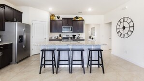 Una cocina moderna con armarios oscuros, un refrigerador de acero inoxidable, un microondas y una isla grande con taburetes de bar.