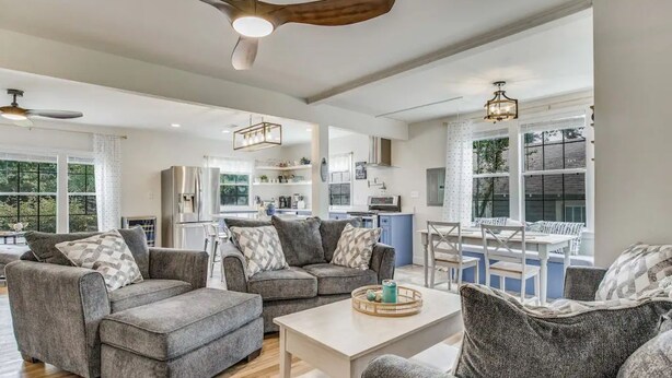 A spacious living area with grey sofas, a white coffee table, and a kitchen in the background. - The East Hill Escape, A Bay View Beachy Cottage (Pensacola)