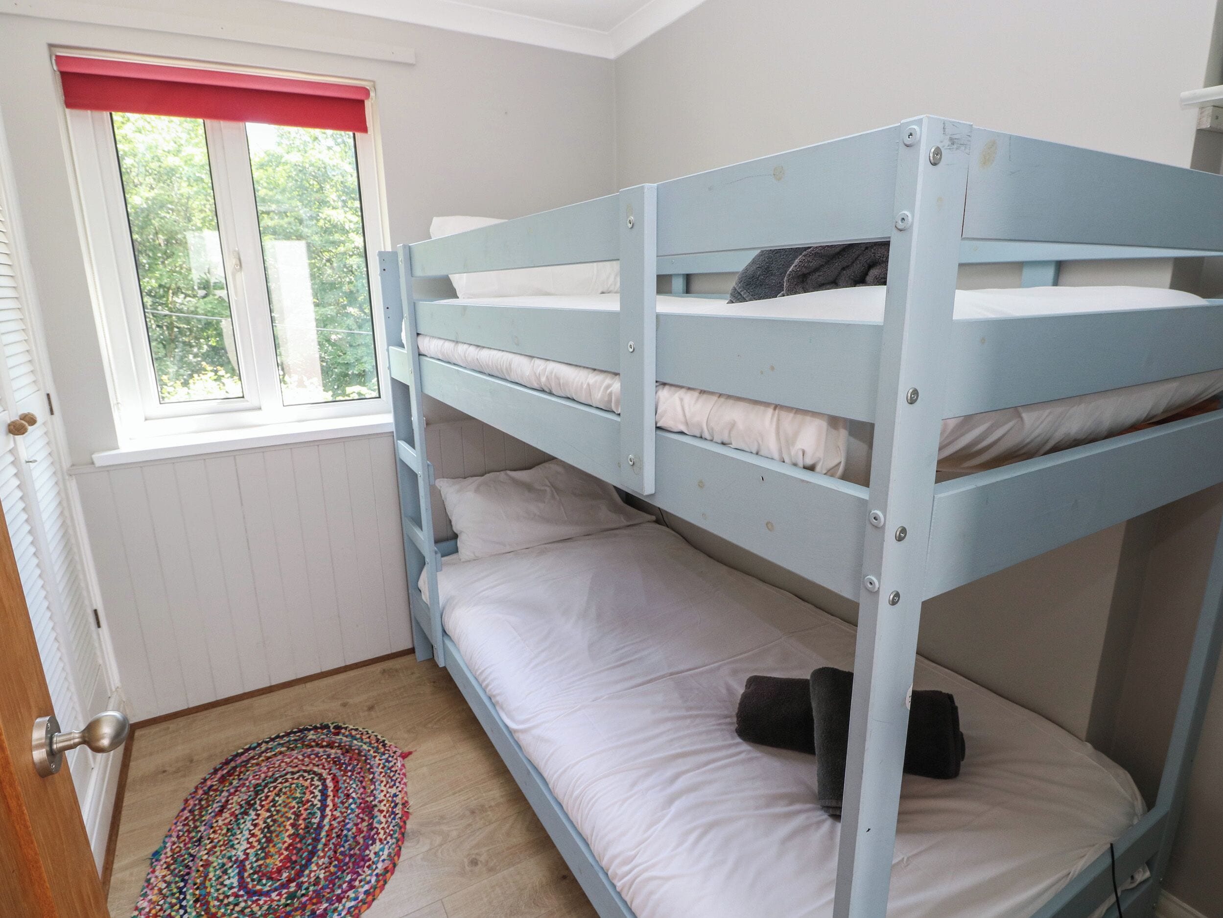 Een slaapkamer met stapelbed, raam, deur en een kleurrijk tapijt.