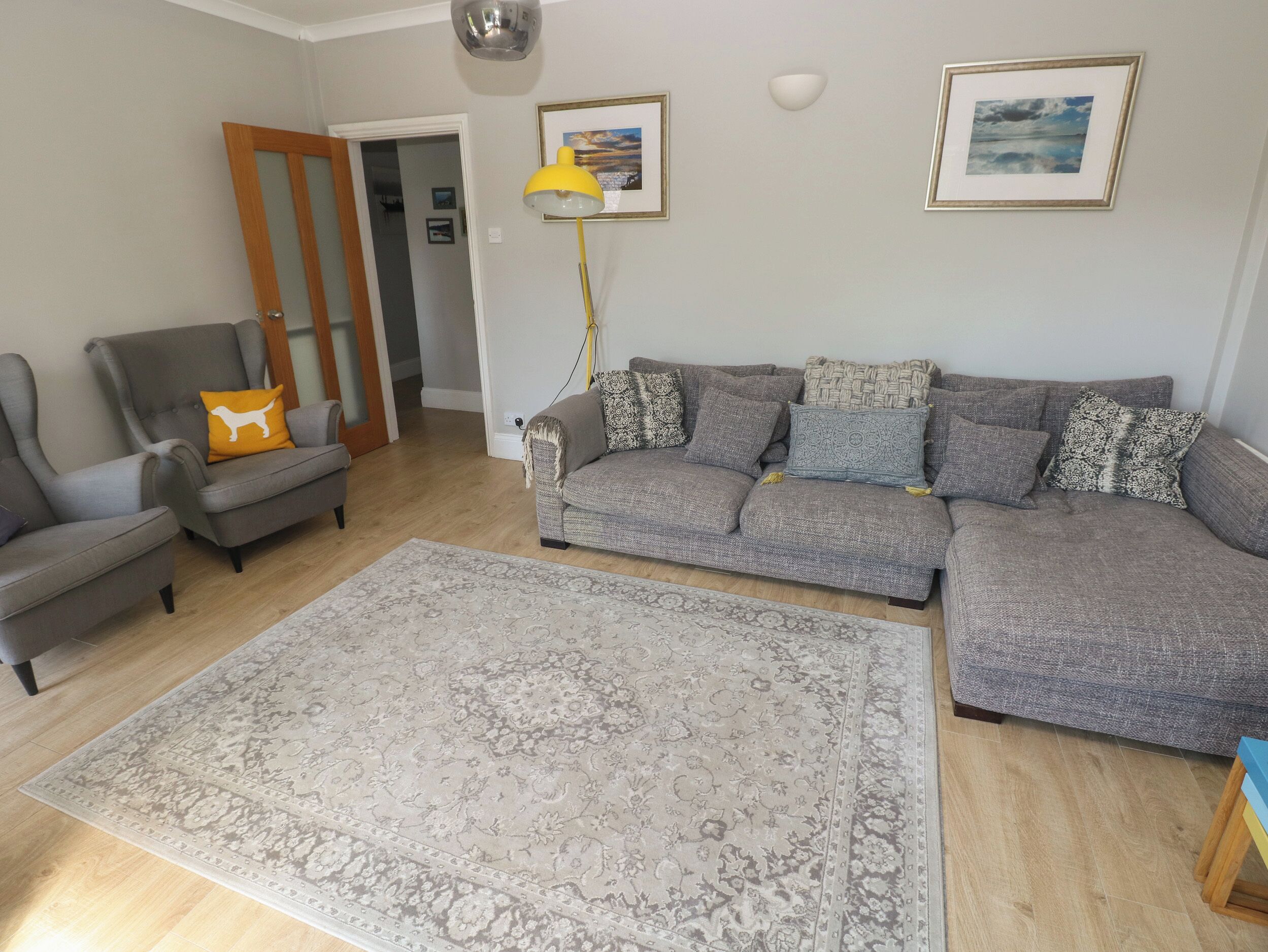 Una sala de estar con un sofá gris, un sillón gris, un tapete estampado y suelo de madera.