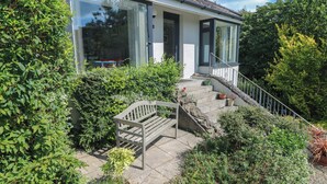 Ein modernes Haus mit einer Steintreppe, die zu einer Holzbank und topfpflanzenführenden Blumenbeeten führt.