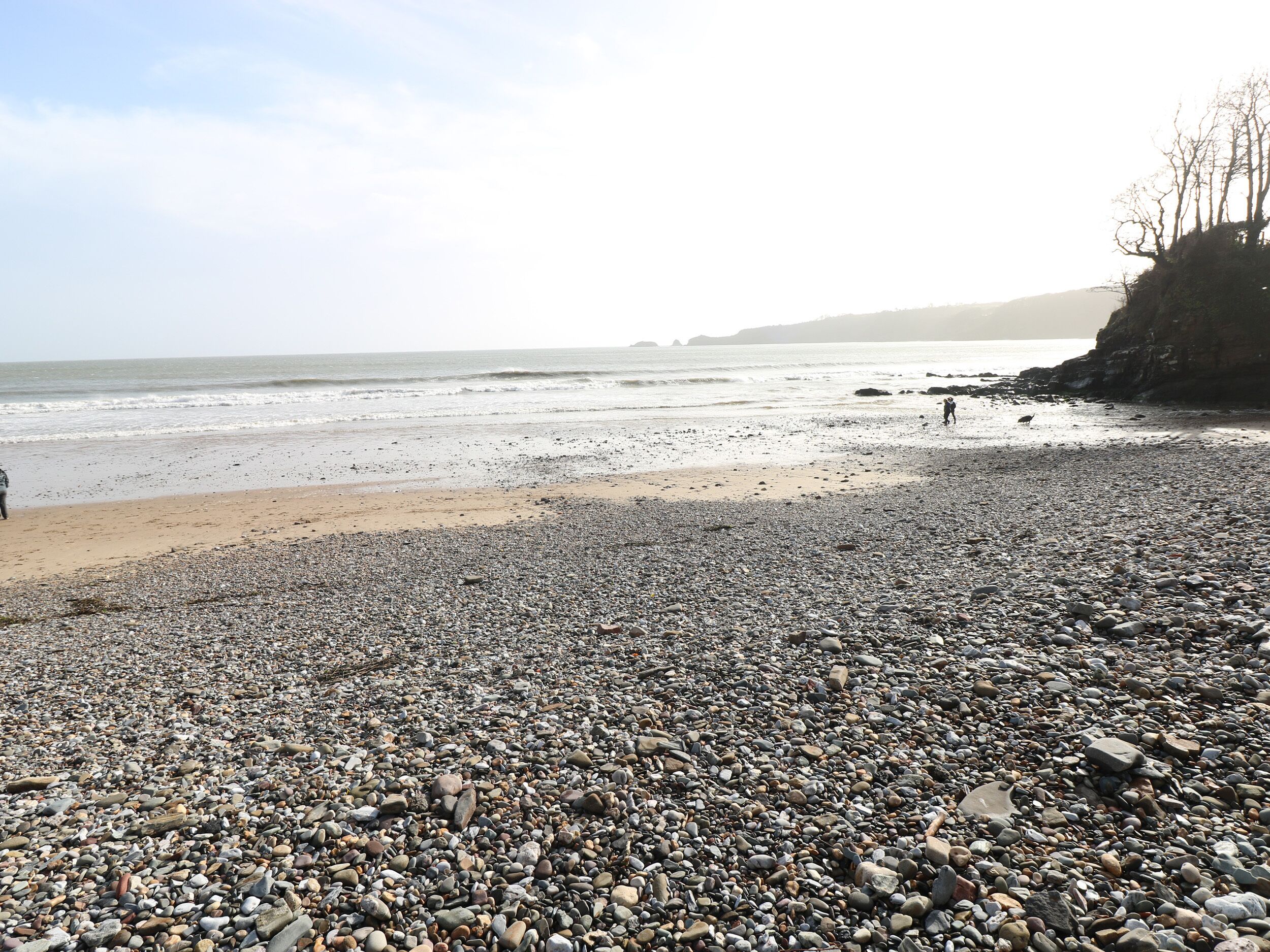 A pebbled beach with a rocky shoreline and a distant view of the sea.