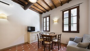 Un comedor con una mesa y sillas de madera, un televisor en un mueble bajo y un sofá.