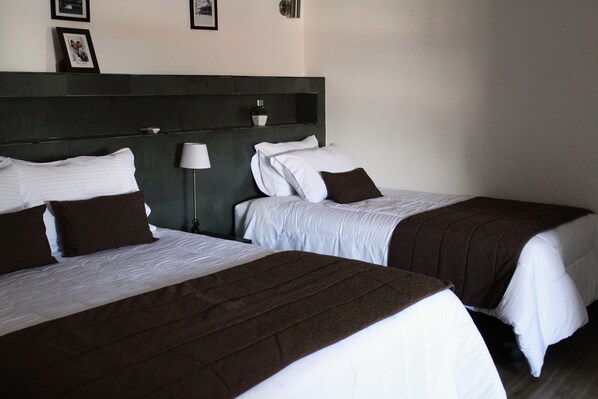 A hotel room with two beds, each with white and brown bedding. There is a bedside table with a lamp, and a small potted plant on the headboard. - HOTEL MACKENNA (Osorno)