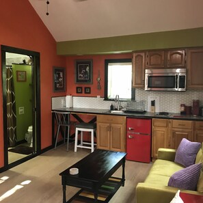 A compact kitchen with a red refrigerator, a microwave, and a sink. There is a small dining area with a table and chairs.