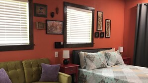 Ein Zimmer mit einem grünen Sofa, einem Bett mit einer Decke, einem Holztisch und zwei Nachttischen mit Lampen.