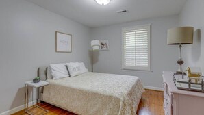 Quarto com cama, mesa de cabeceira, abajur e janela com persianas.
