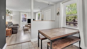 Une pièce avec une table en bois, un ventilateur de plafond, un canapé, un téléviseur et une fenêtre donnant sur un paysage verdoyant.