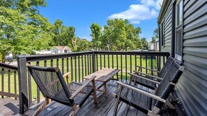 Une terrasse en bois avec une table et des chaises, une rambarde et une vue sur une pelouse verdoyante et des arbres.
