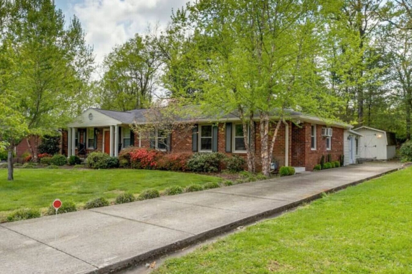 A single-story brick house with a front porch, a small attached garage, and a well-maintained lawn.