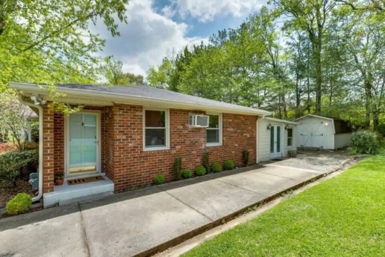 A single-story brick house with a front porch, a garage, and a small shed in the backyard.