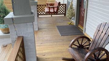 A covered porch with a wooden floor, a swing chair, a wooden bench, and a barrel.