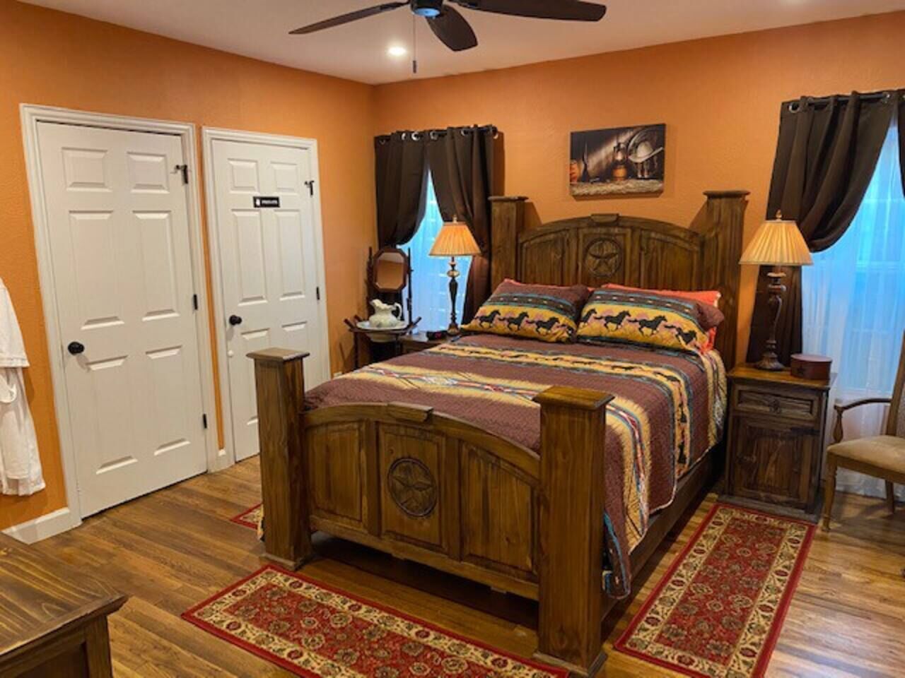A bedroom with a wooden bed, two doors, a ceiling fan, and a nightstand with a lamp.