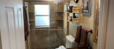 A bathroom with a glass-enclosed shower, a toilet, and a sink.