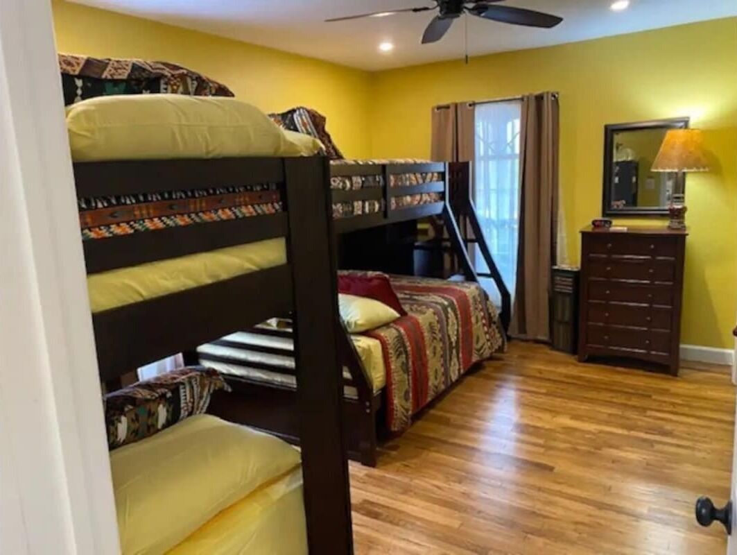 Une chambre avec des lits superposés, une commode, un miroir et un ventilateur de plafond.