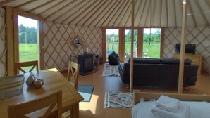 L’intérieur d’une yourte, avec une table en bois, des chaises, un canapé, un téléviseur et une cheminée.