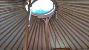 L’intérieur d’une yourte, avec une lucarne circulaire, des poutres en bois et une fenêtre.