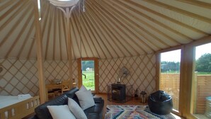 L’intérieur chaleureux d’une yourte, avec un canapé en cuir noir, un tapis à motifs et un poêle à bois.