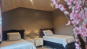 Quarto com duas camas, uma mesa de cabeceira com abajur e uma planta decorativa.