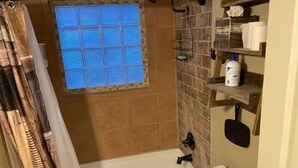 Un baño con bañera, una ventana de vidrio azulado, una zona de ducha y un inodoro.