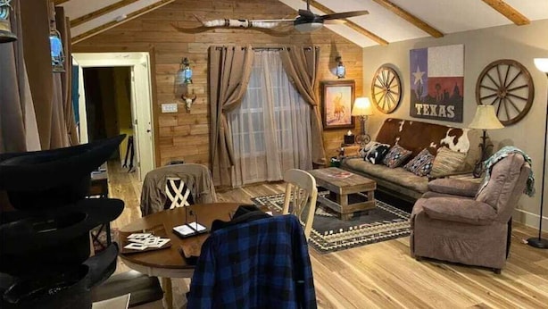 Una sala de estar acogedora con vigas de madera, un ventilador de techo, un sofá, una mesa de centro y una chimenea.