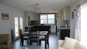 Une cuisine moderne avec des meubles de couleur sombre, un coin repas avec une table et des chaises bleues, et un canapé blanc agrémenté d’un coussin décoratif.