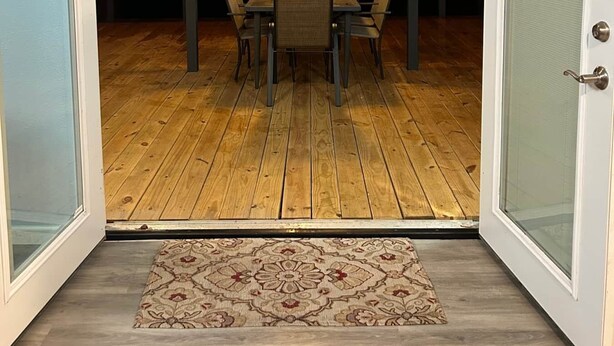Une porte ouverte donne sur un patio abrité, équipé d’une table et de chaises, d’un plancher en bois et de guirlandes lumineuses.