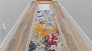 Un pasillo con piso de madera, un tapete colorido y una puerta con paneles horizontales.