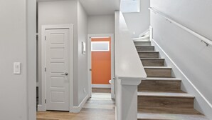 Una escalera de madera con barandillas blancas que conduce a una puerta anaranjada al final.