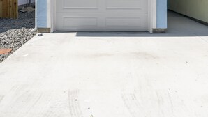 Una casa de dos pisos con una puerta de garaje blanca, un balcón con barandillas blancas y un pequeño ventanal circular sobre la puerta.