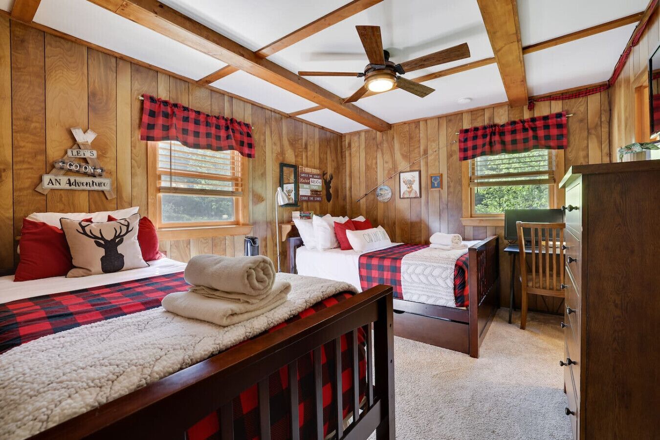 A room with two beds, wooden walls, a ceiling fan, and a window with a view.