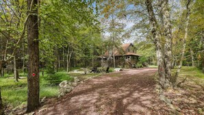Un chalet rustique entouré d’une zone boisée, avec un sentier de terre qui y mène.