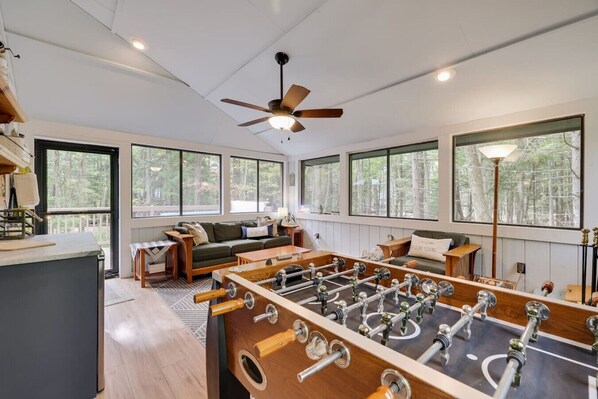 A spacious room with a foosball table, large windows, and a ceiling fan.